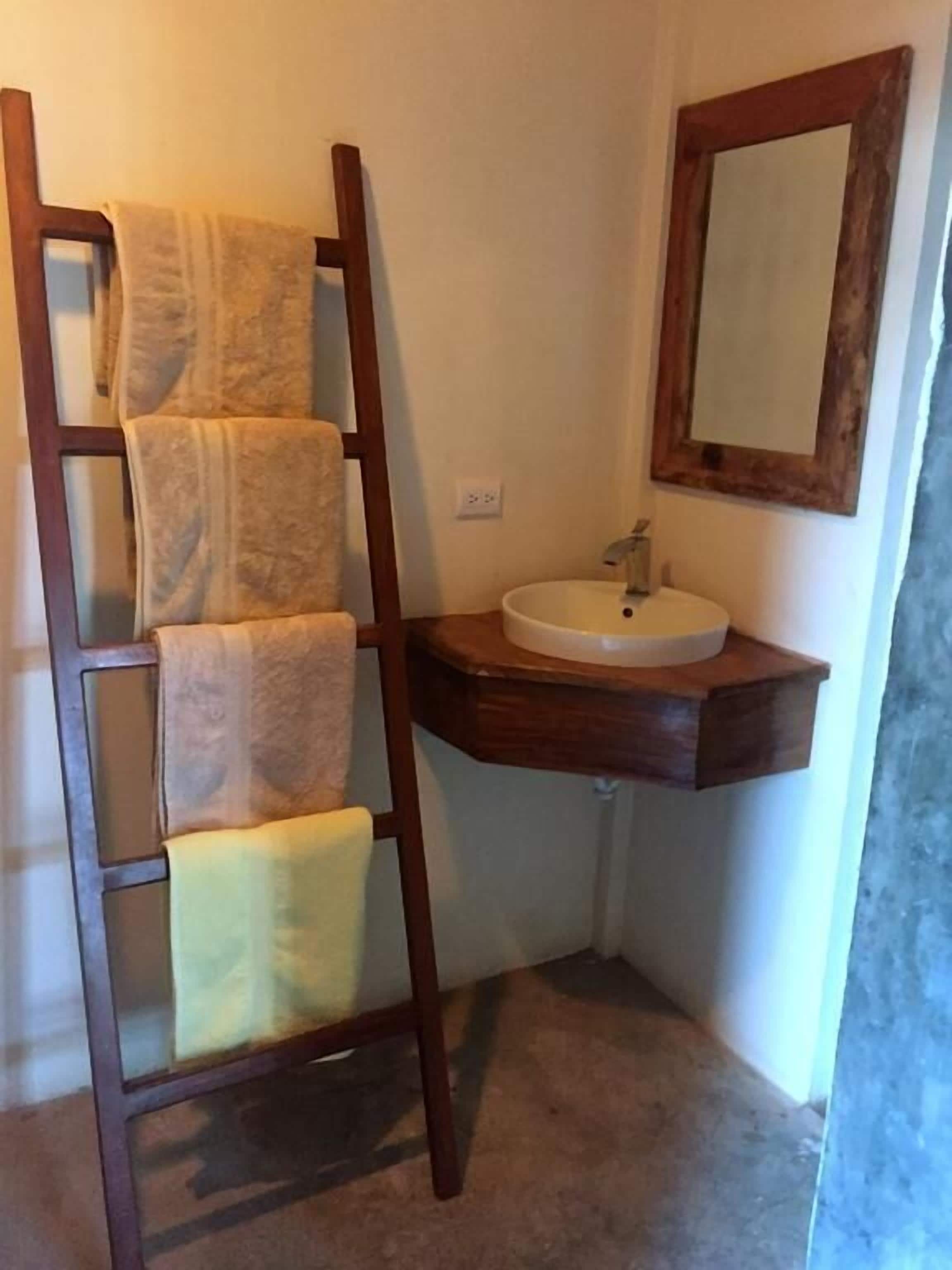 A bathroom with a wooden ladder holding towels, a sink, and a mirror.