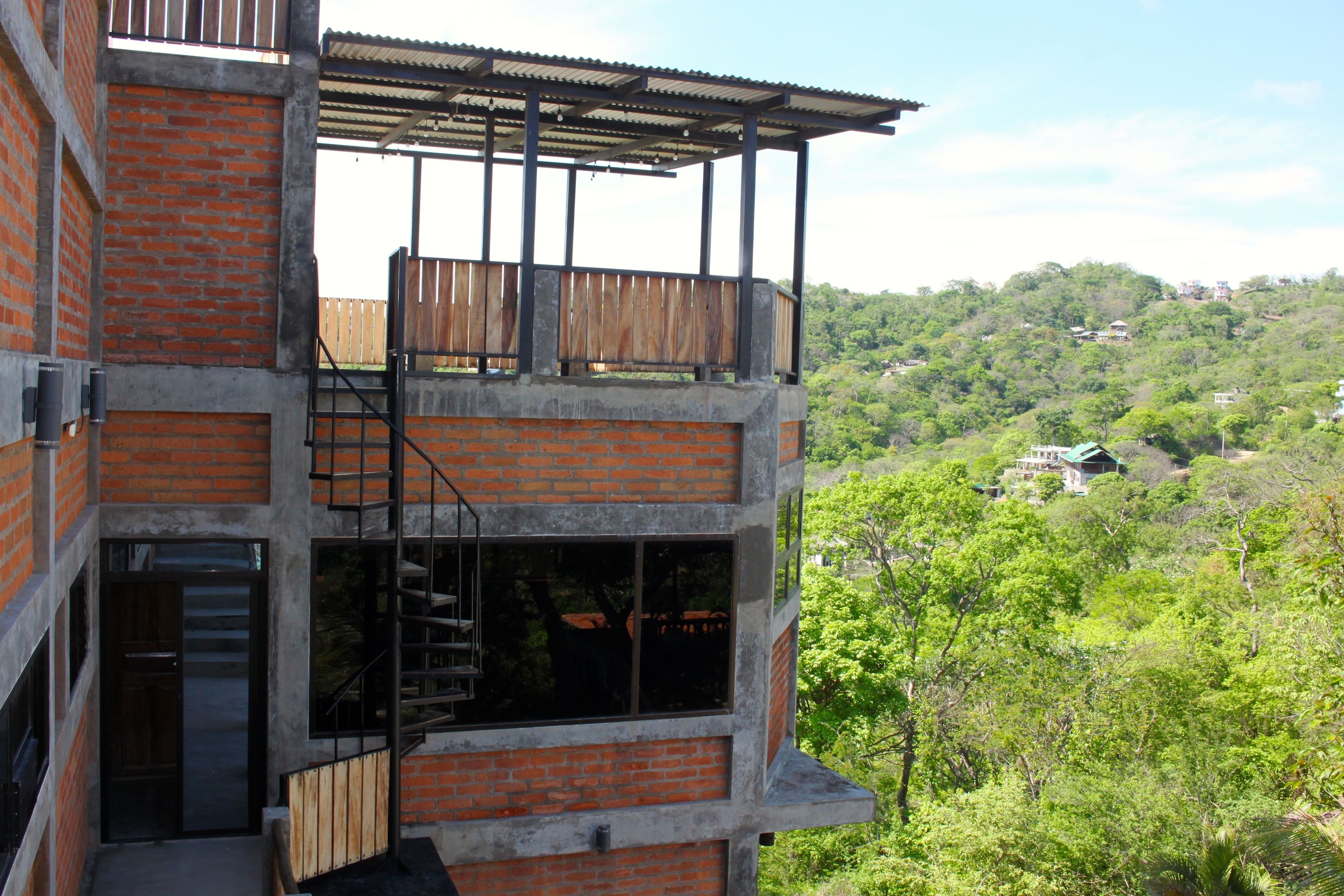 A multi-story building with a balcony, a staircase, and a view of a forested hillside.