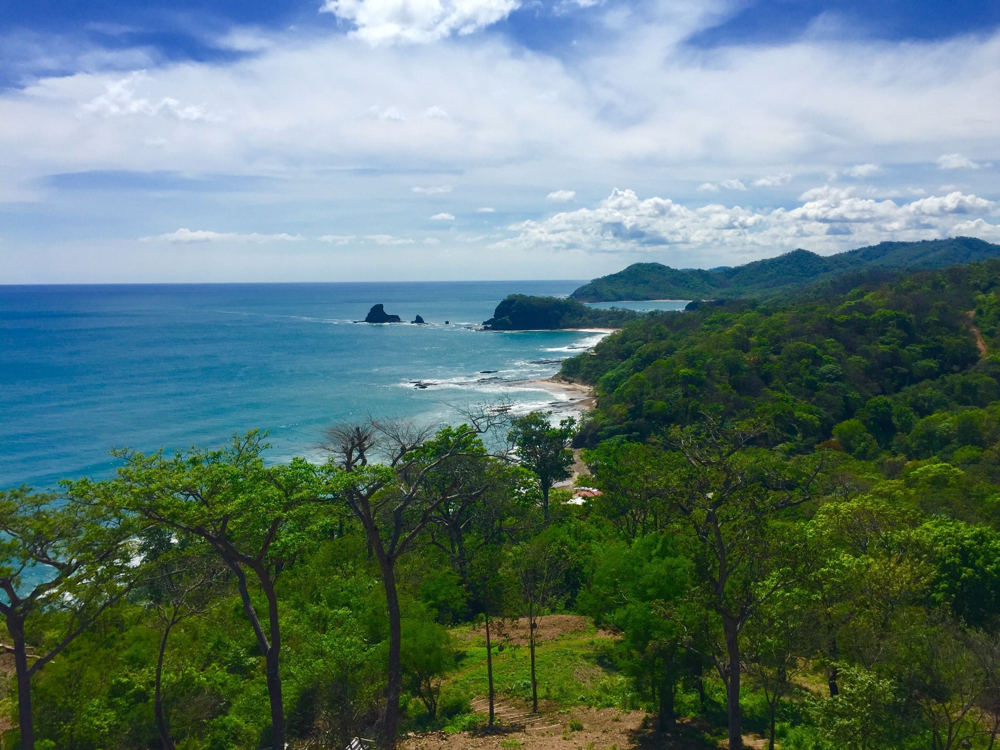 A coastal landscape with a beach, forested hills, and rocky outcrops.