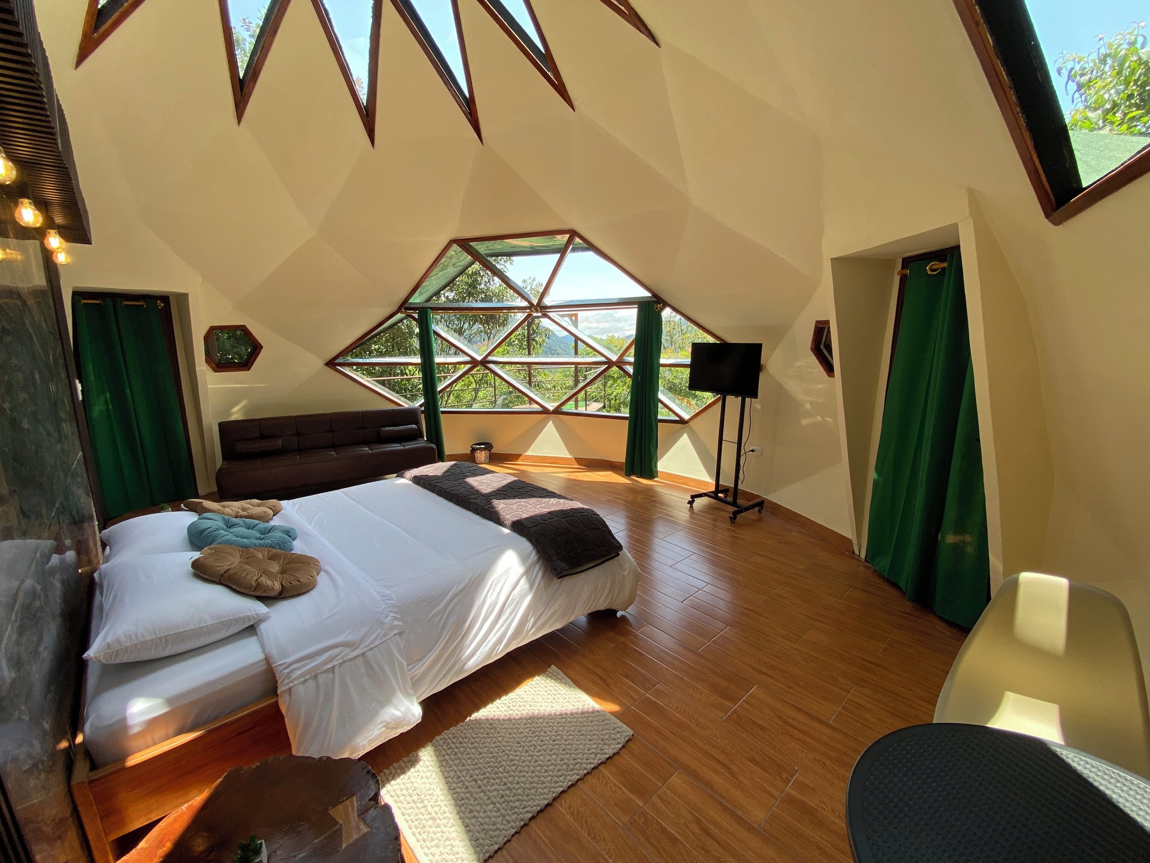 A bedroom with a large bed, a sofa, a TV, and a view through a window.
