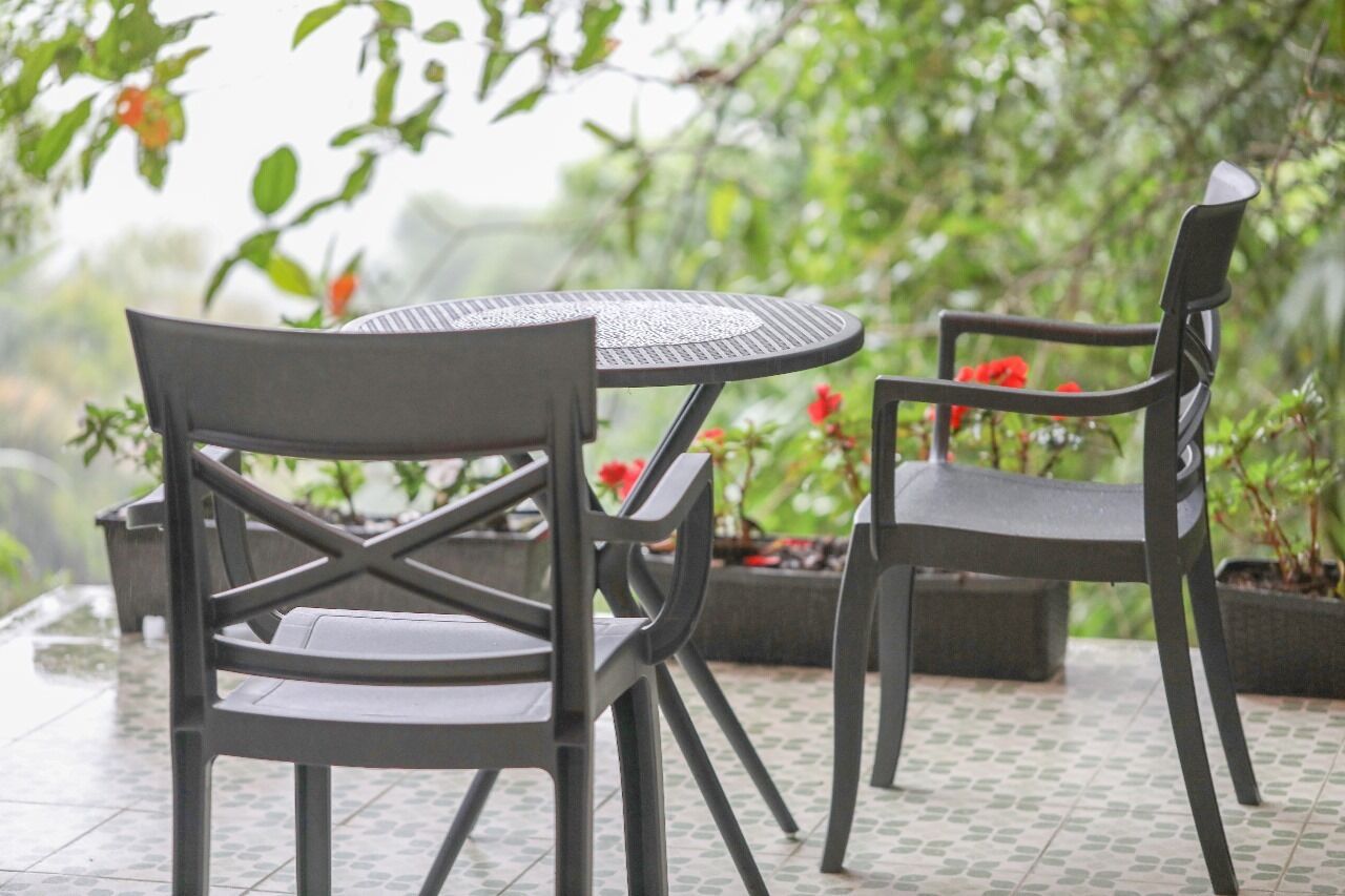 A patio area with two chairs and a table, surrounded by potted plants and greenery.