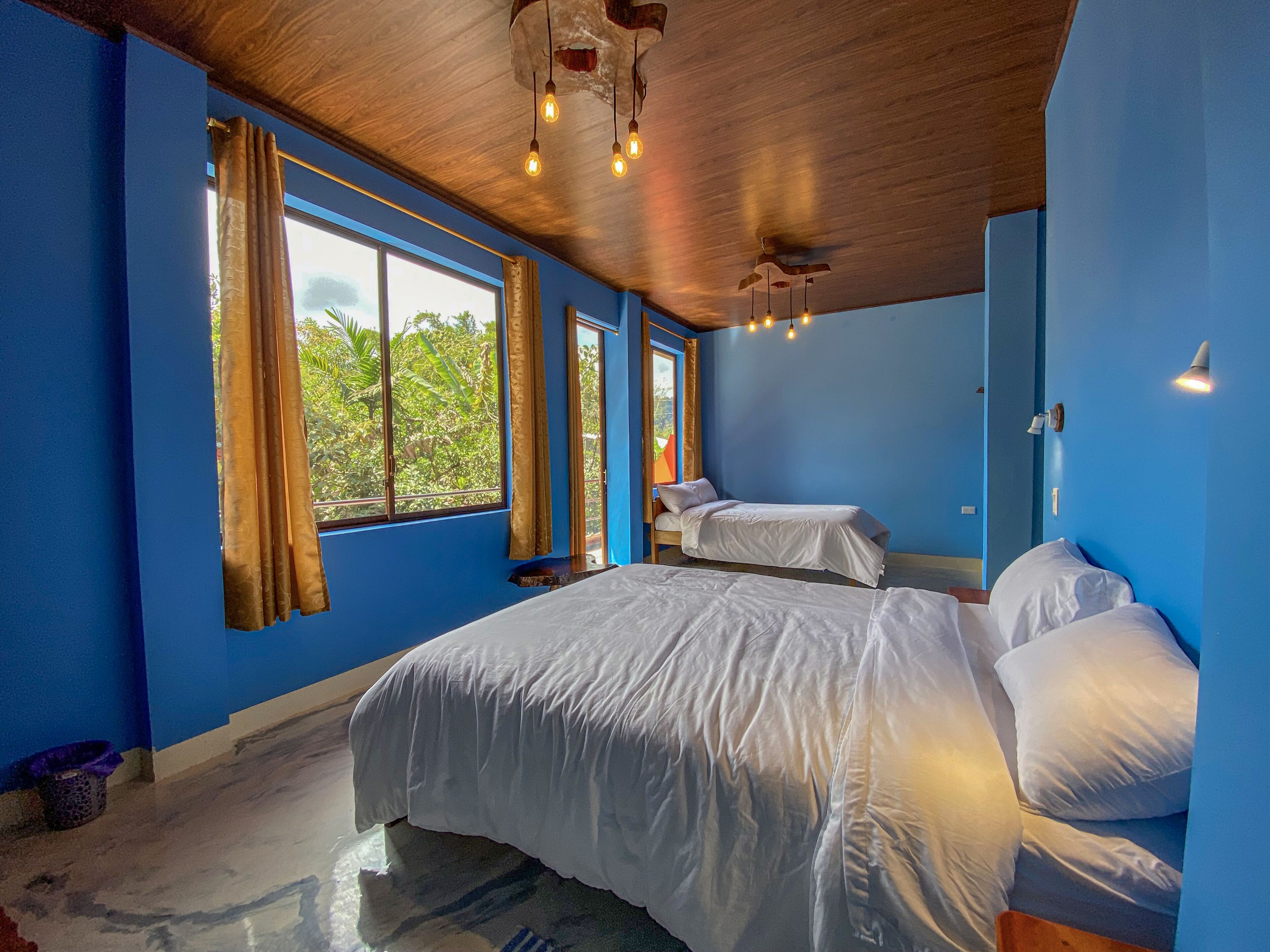 Una habitación con dos camas, ventanas amplias y techo con vigas a la vista y luces colgantes.