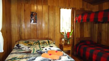 A wooden cabin room with a bed featuring a panda print, a small table with a vase of flowers, and a window with curtains.
