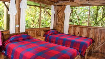 A wooden cabin with two beds, each with a red and blue checkered blanket, and white curtains.