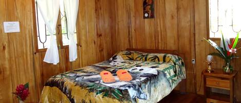 Una habitación de madera con una cama, una mesita de noche con una lámpara y una ventana con cortinas.