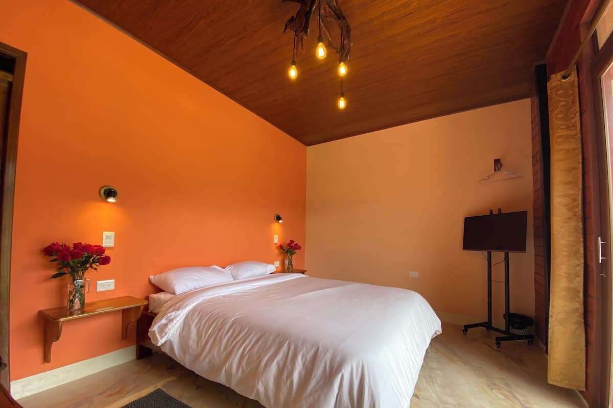 A bedroom with a wooden ceiling, a bed with white bedding, two bedside tables with lamps, and a flat-screen TV on a stand.
