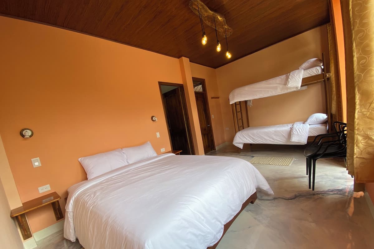 A hotel room with a large bed, a smaller bed on a bunk, a wooden ceiling, and a light fixture.