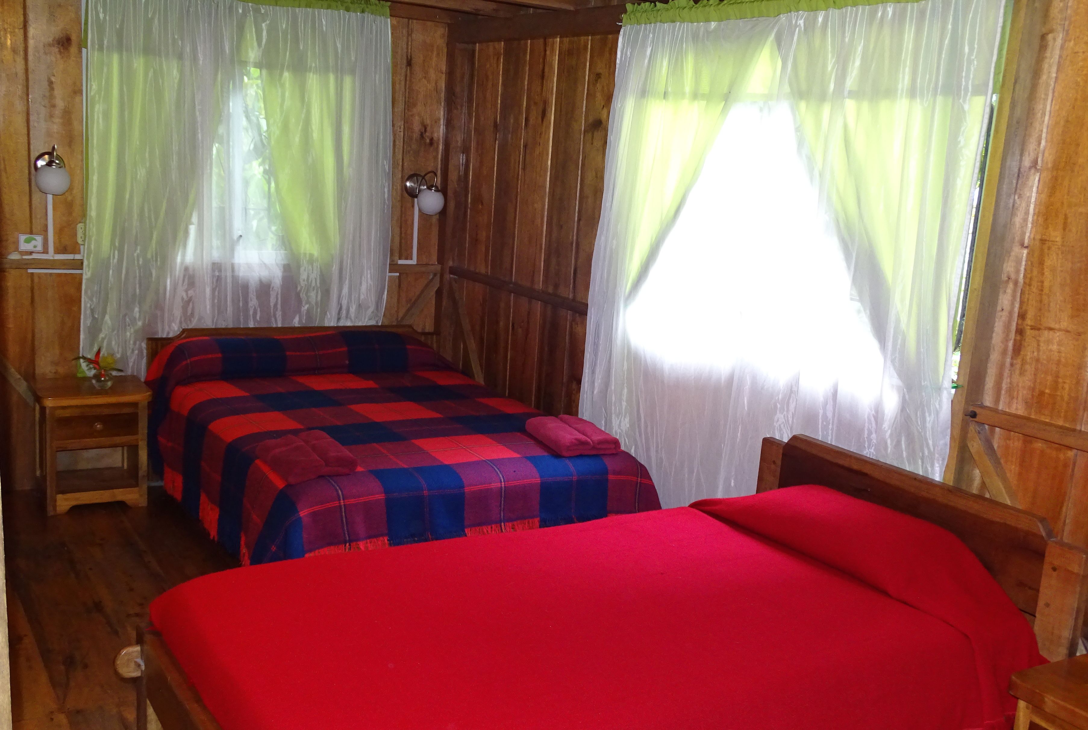 Een houten kamer met twee bedden, waarvan één met een rode deken en de ander met een ruitbeddegoed.