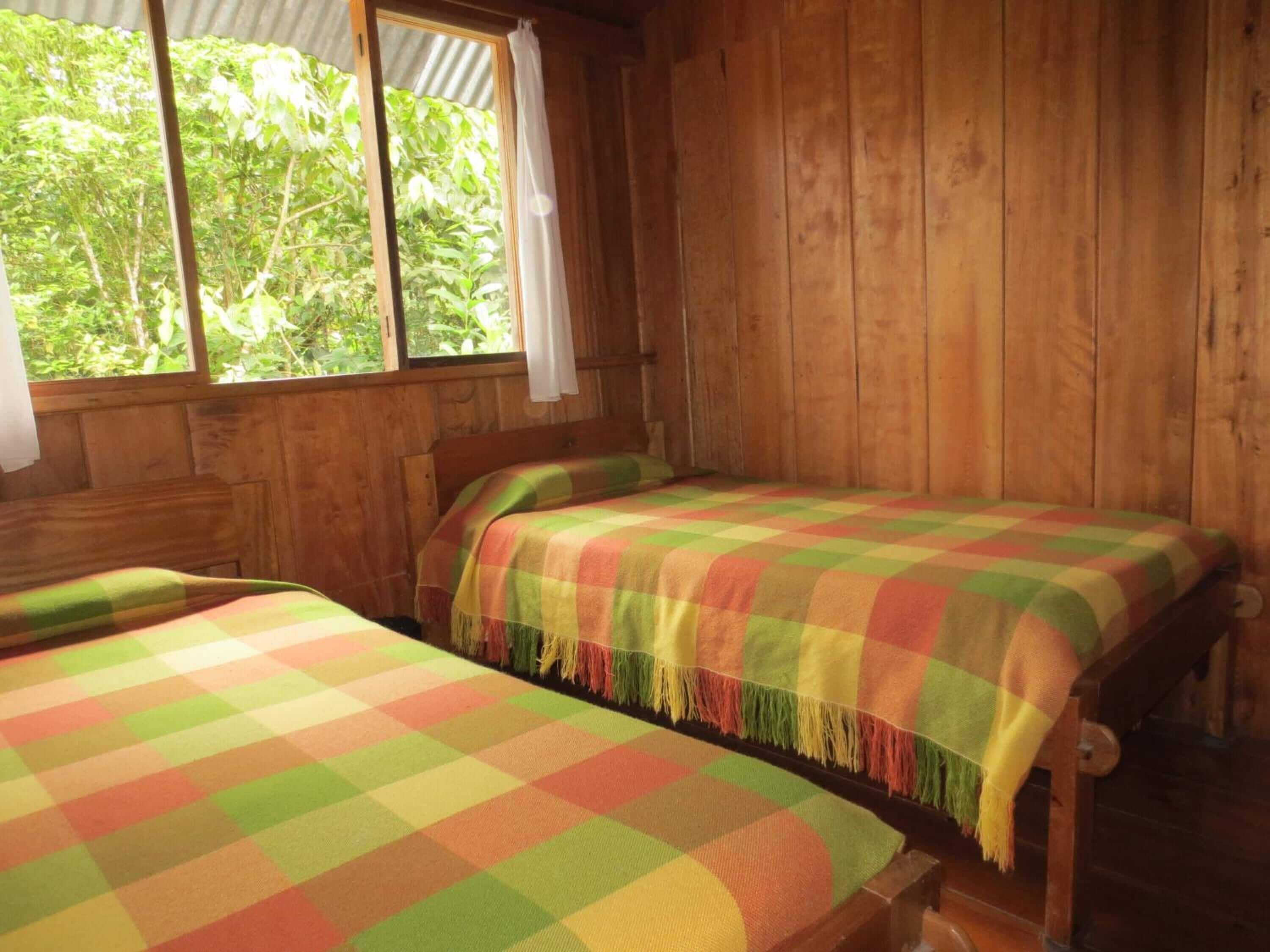 Een houten hut met twee bedden, elk met een kleurrijke geruit dekbedsprei.