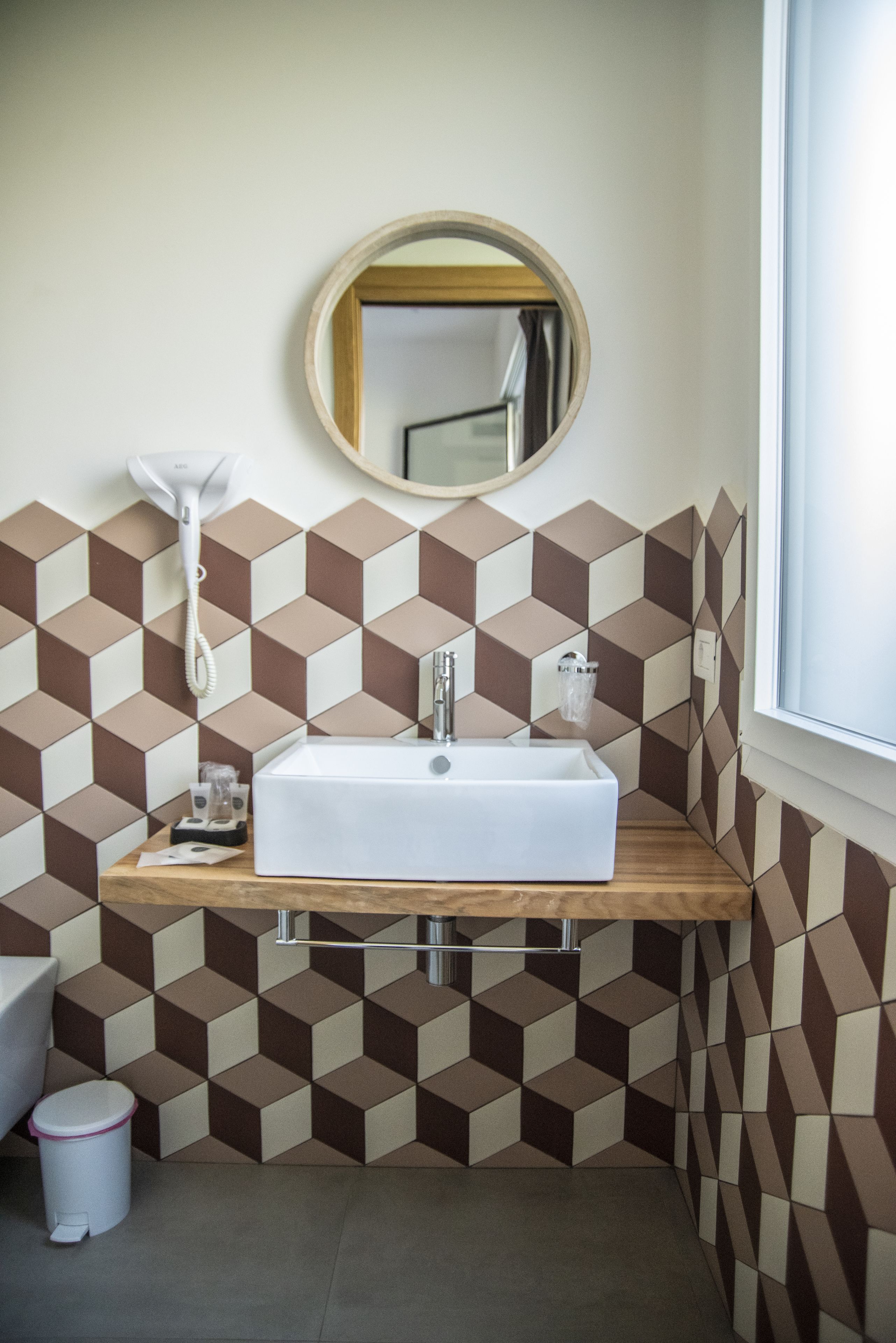 Un baño con un lavamanos blanco, un espejo redondo y paredes con motivos geométricos.