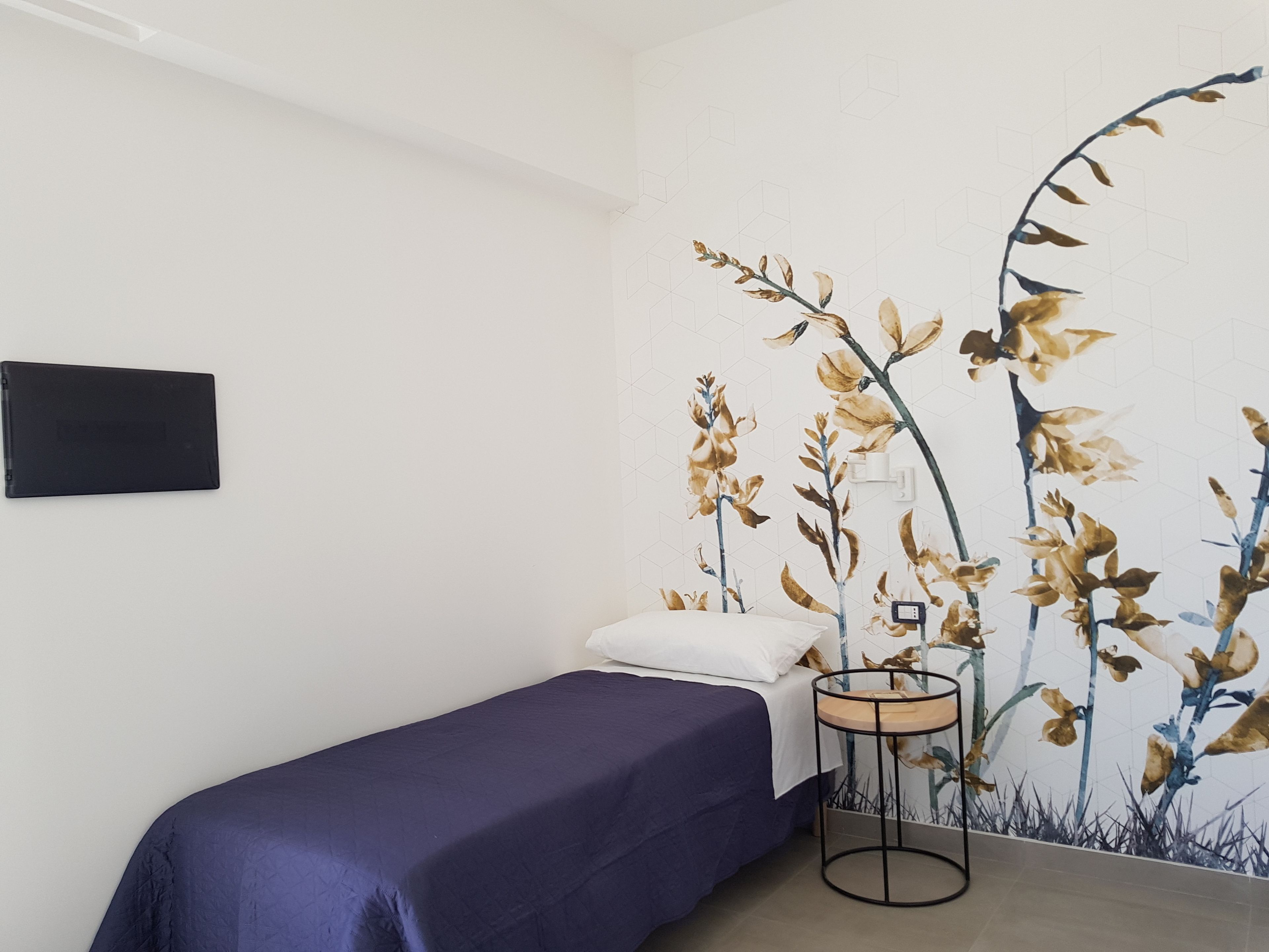 Ein Schlafzimmer mit einem Bett, einem kleinen Nachttisch und einem an der Wand befestigten Fernseher.
