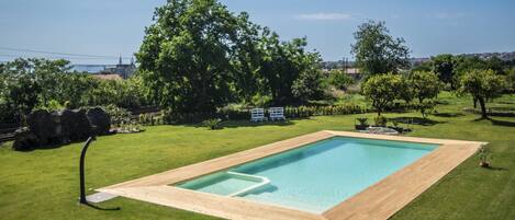 A rectangular swimming pool with a wooden deck, surrounded by well-maintained grass and trees.