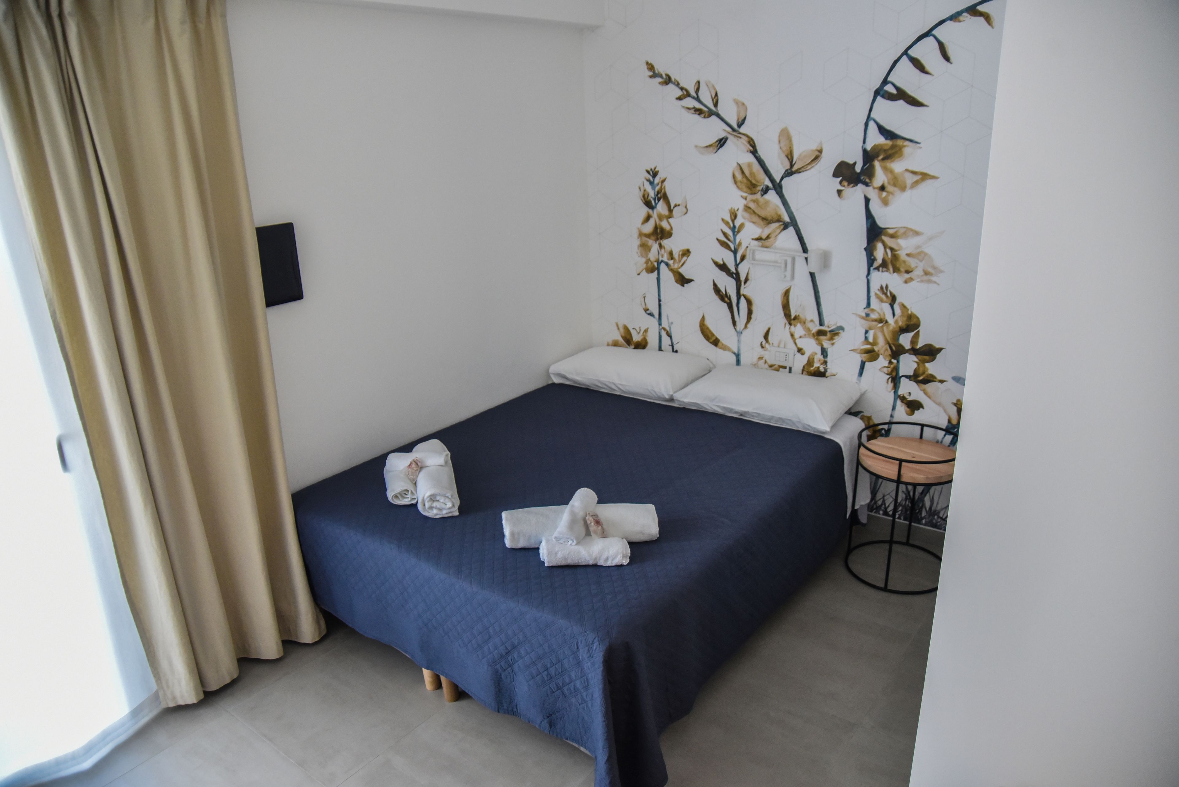 A neatly made bed with a dark blue bedspread and two rolled towels on it.