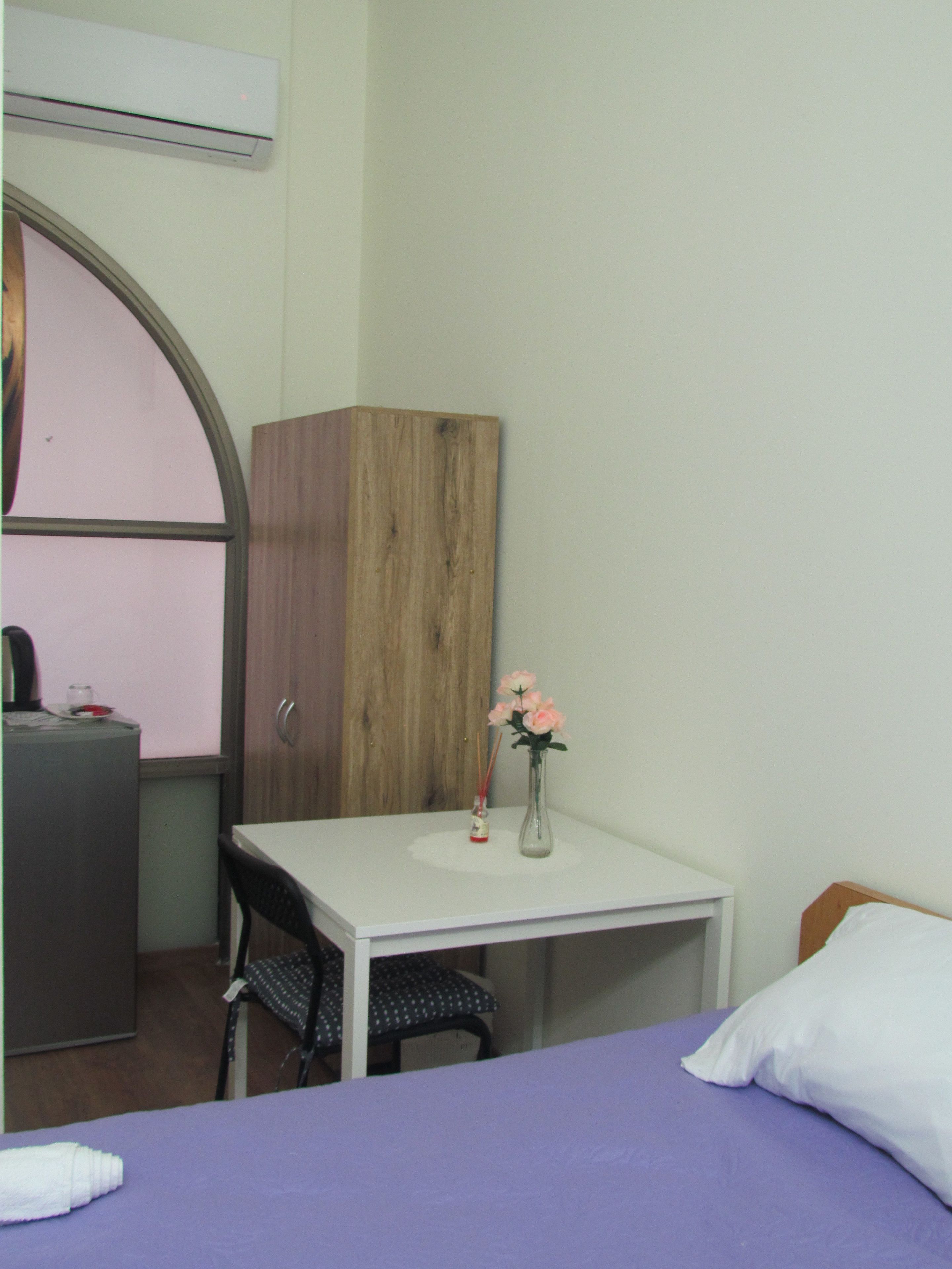 A small room with a bed, a desk, and a chair. There is a cabinet and a vase with flowers on the desk.