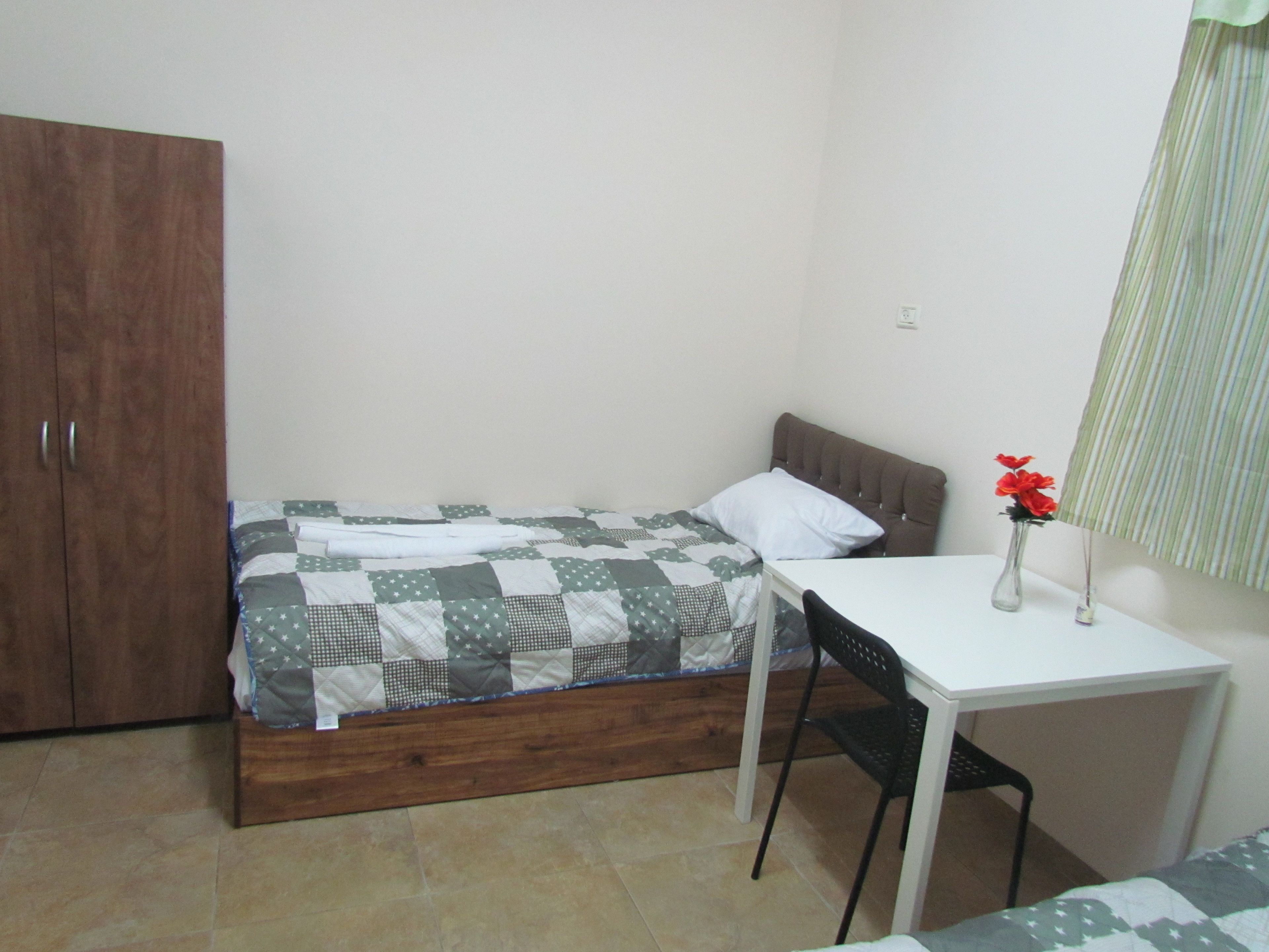 A small, neatly arranged bedroom with a bed, a desk, and a chair.