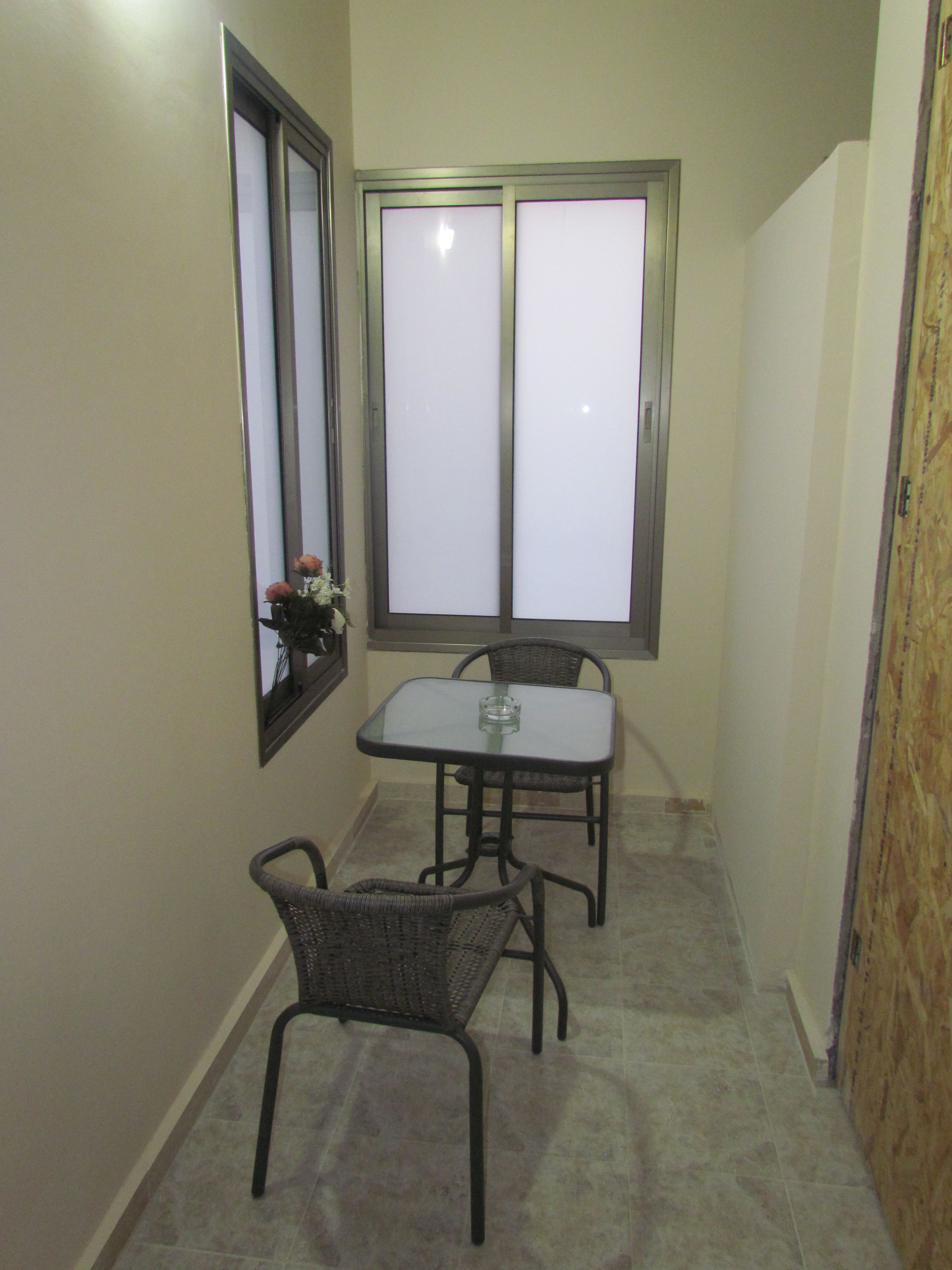 Una habitación pequeña con una mesa, dos sillas, un ventanal y un espejo en la pared.