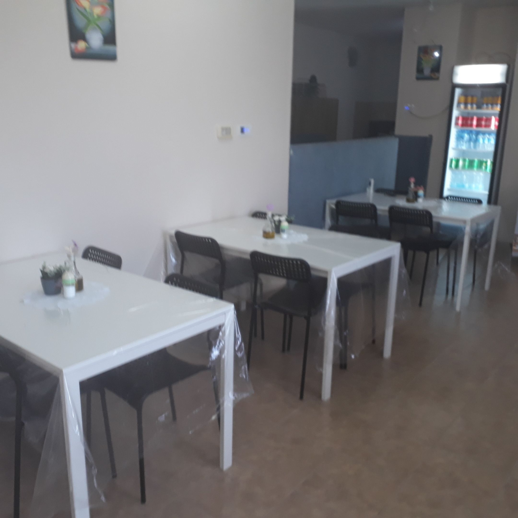 Een eethoek met tafels en stoelen, een koelkast en een schilderij aan de muur.