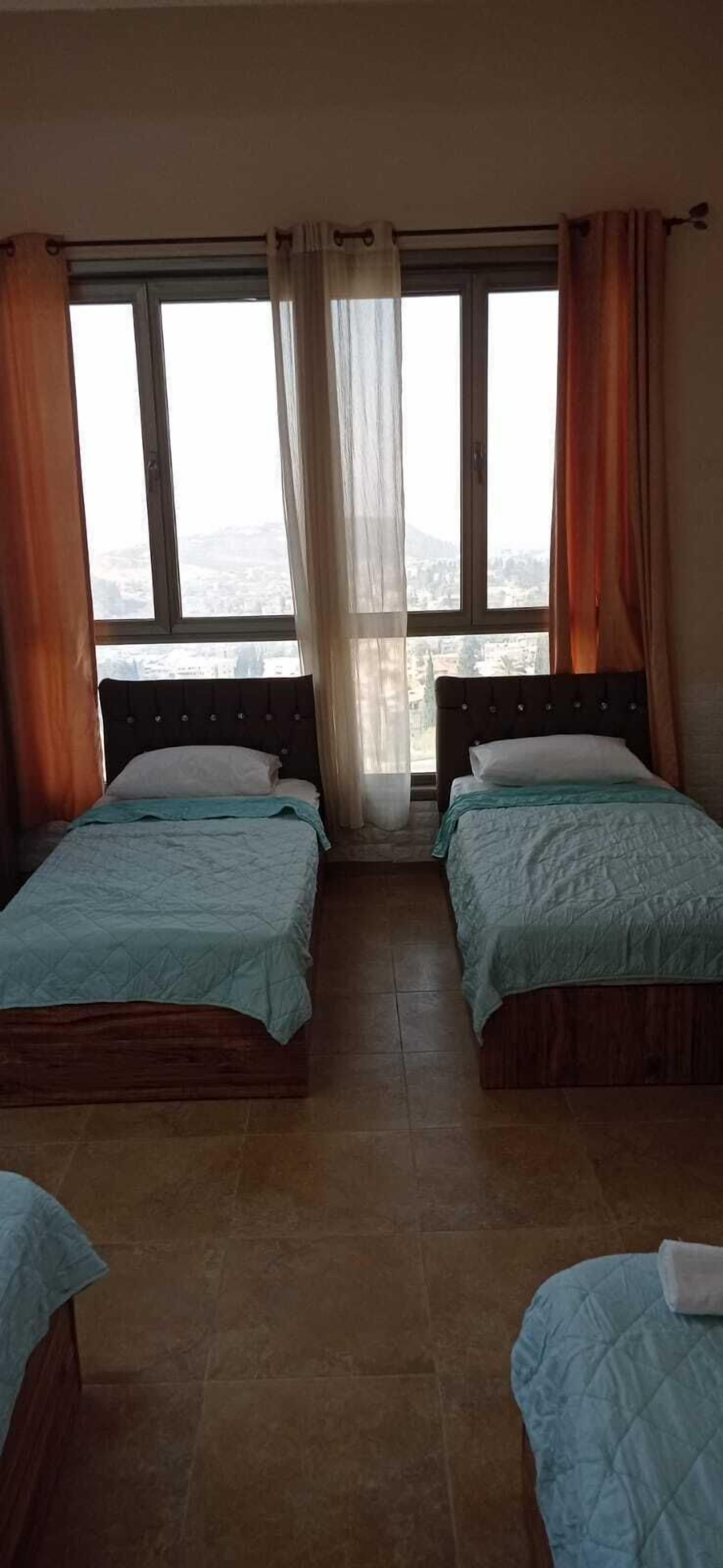 Une chambre avec deux lits, une grande fenêtre avec des rideaux et une vue sur le paysage urbain.