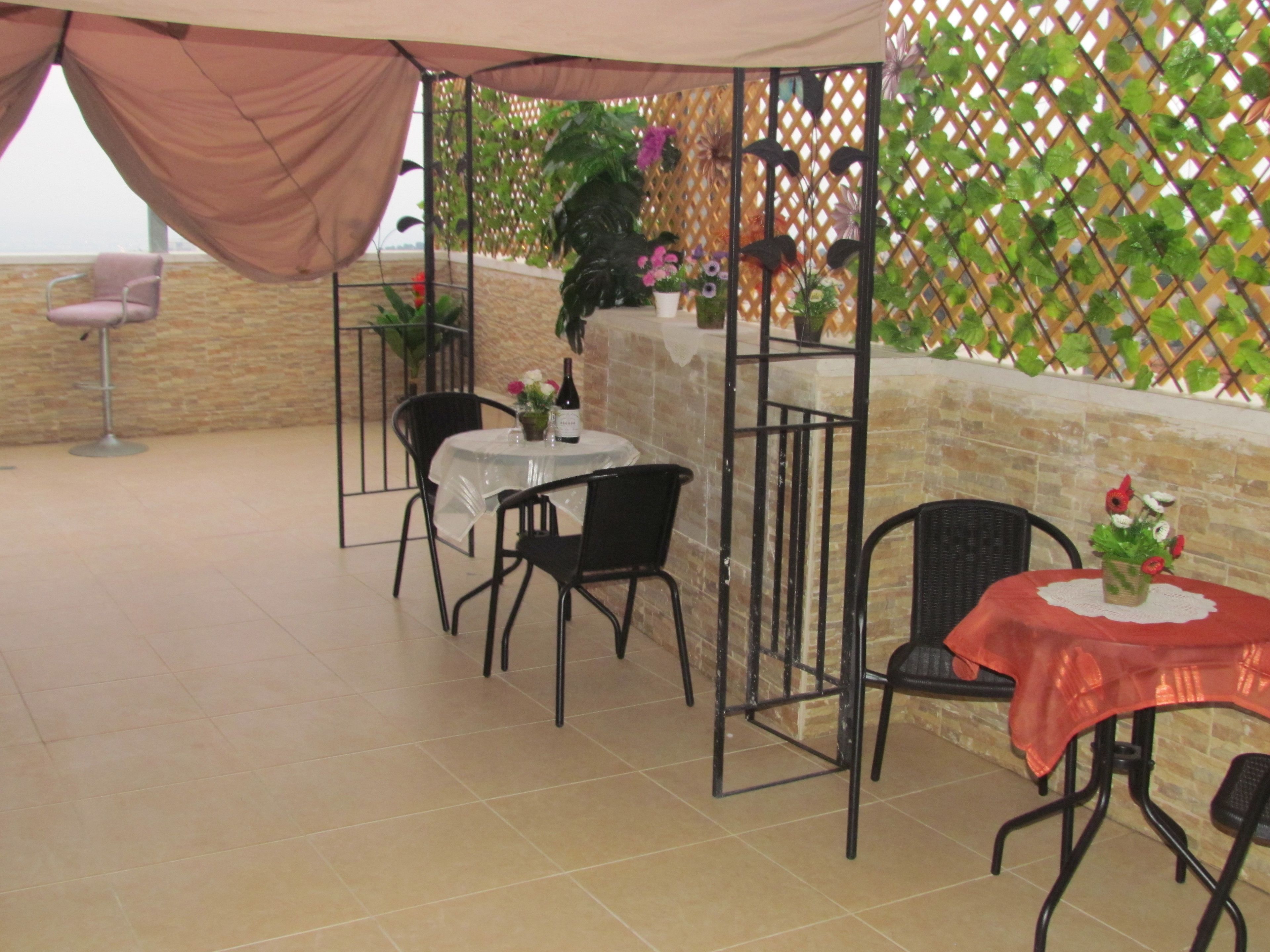 Une terrasse extérieure avec une table et des chaises, un espace salon abrité et une clôture décorative agrémentée de plantes.