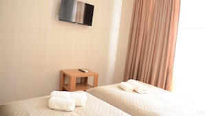 Een hotelkamer met twee bedden, een aan de muur bevestigde televisie, een klein houten tafeltje en een raam met gordijnen.