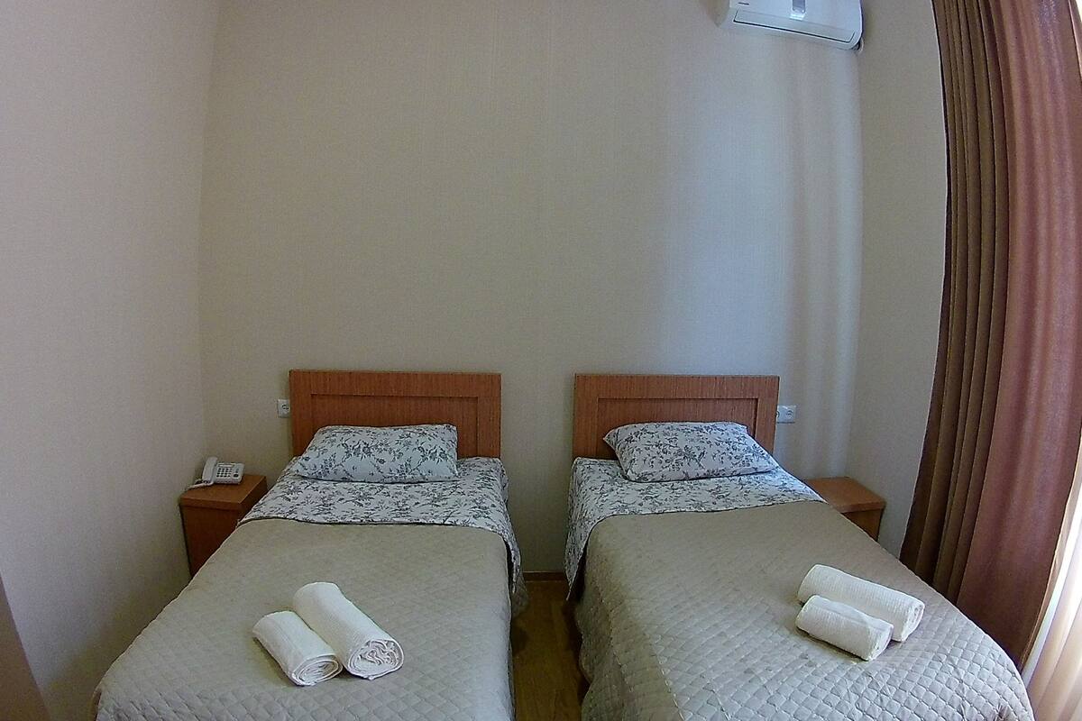 Ein Hotelzimmer mit zwei Einzelbetten, einem Nachttischtelefon und einem mit Vorhängen versehenen Fenster.