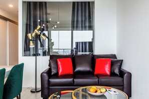 Een moderne woonkamer met een leren bank, rode kussens, een glazen salontafel met fruit, en een vloerlamp.