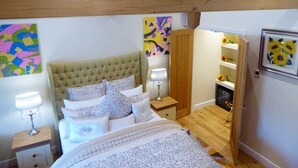 A bedroom with a tufted headboard, a bed with multiple pillows, a bedside table with a lamp, and a wooden floor. - Handywater Cottage B&B (Henley-on-Thames)