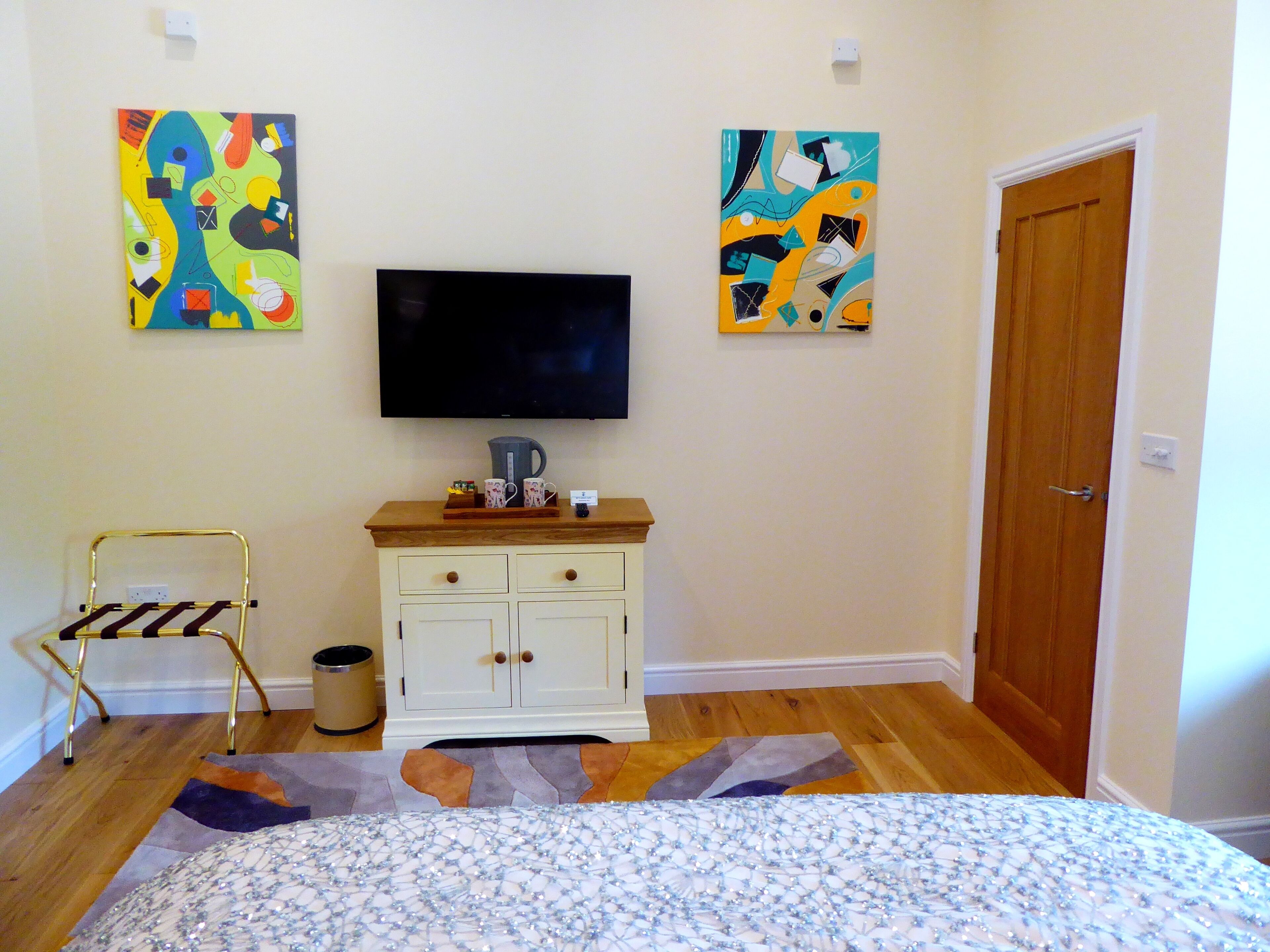 A bedroom with a bed, a TV, a cabinet, and two abstract paintings on the wall.