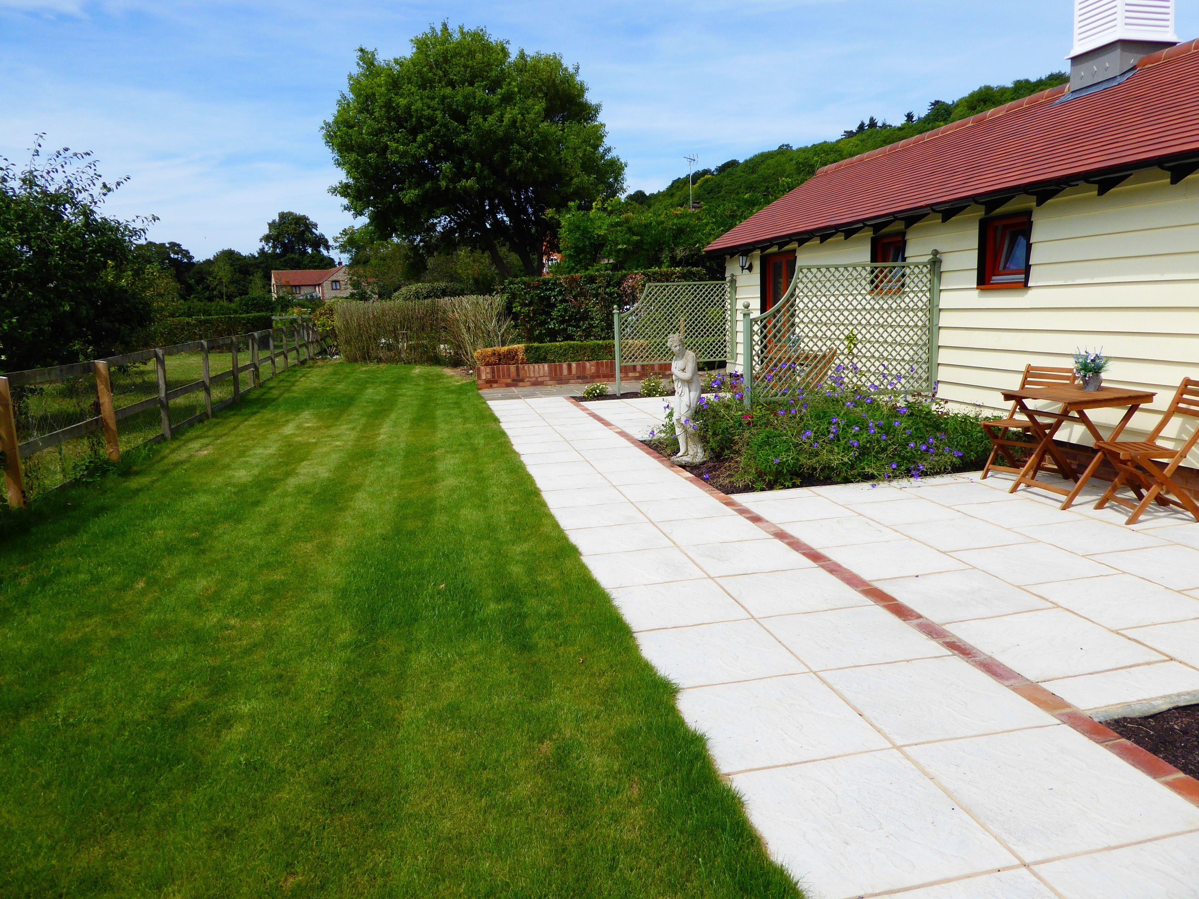 A well-maintained garden with a lawn, a patio area with a table and chairs, and a fence.