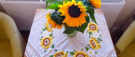 A table with a white tablecloth featuring embroidered sunflowers, a vase with sunflowers, and a radiator in the background.