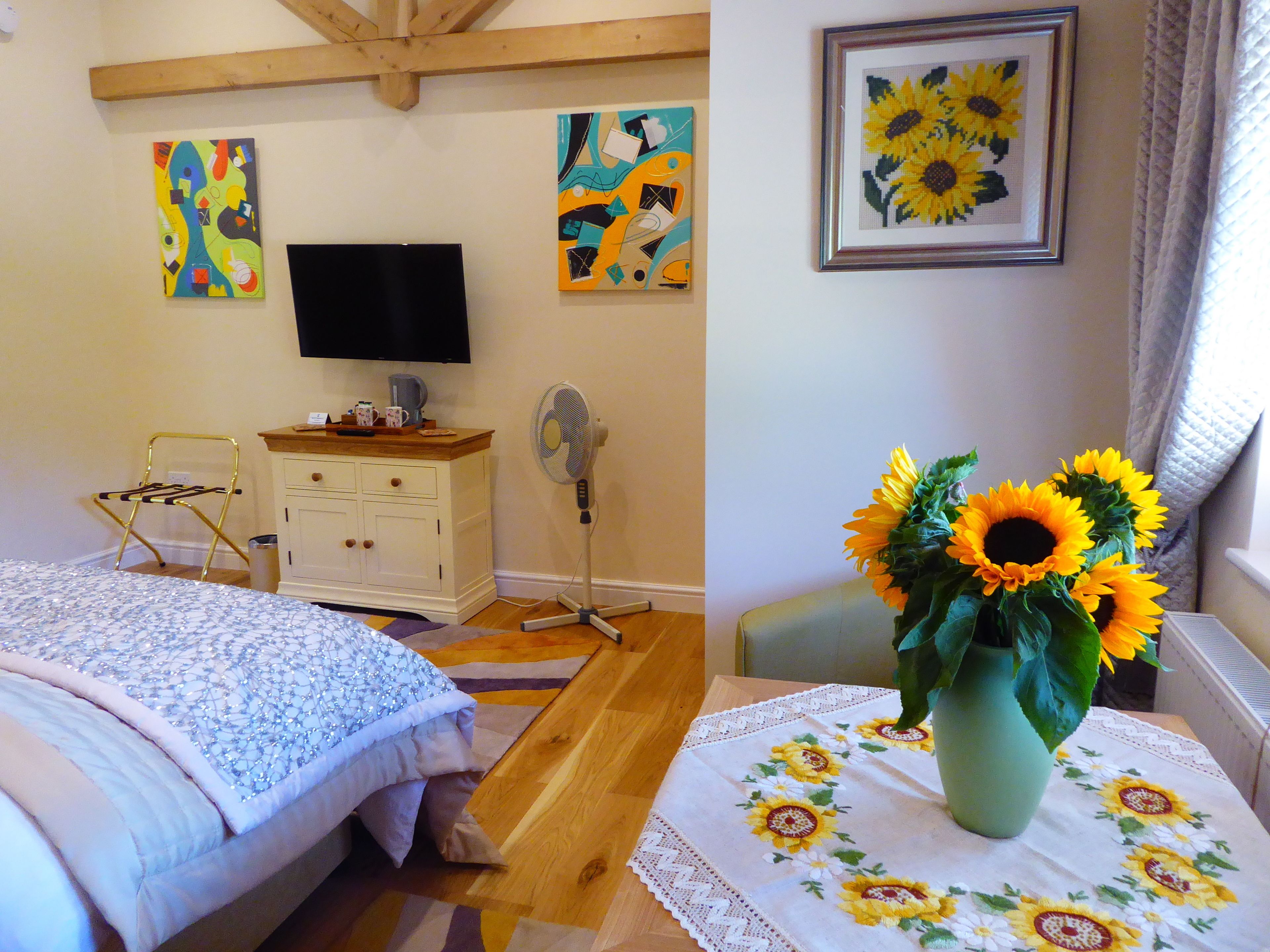 Une chambre à coucher avec un lit, une commode, un téléviseur et un vase rempli de tournesols.