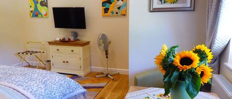 A bedroom with a bed, a dresser, a television, and a vase of sunflowers.