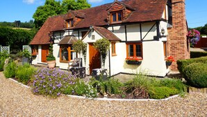 A traditional half-timbered house with a chimney, a front porch, and a garden with gravel paths and flowering plants. - Handywater Cottage B&B (Henley-on-Thames)