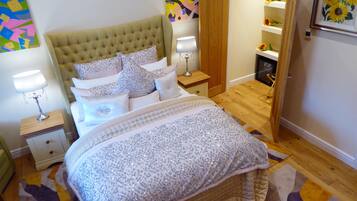 Une chambre à coucher avec une tête de lit capitonnée, un lit recouvert d’un tissu à paillettes, une table de chevet avec une lampe et un plancher en bois.