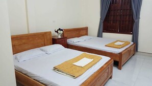Una habitación de hotel con dos camas de madera, ropa de cama blanca y una mesita con un florero.