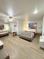 Habitación de hotel con dos camas, ventilador de techo, un cuadro de un paisaje y una mesita.