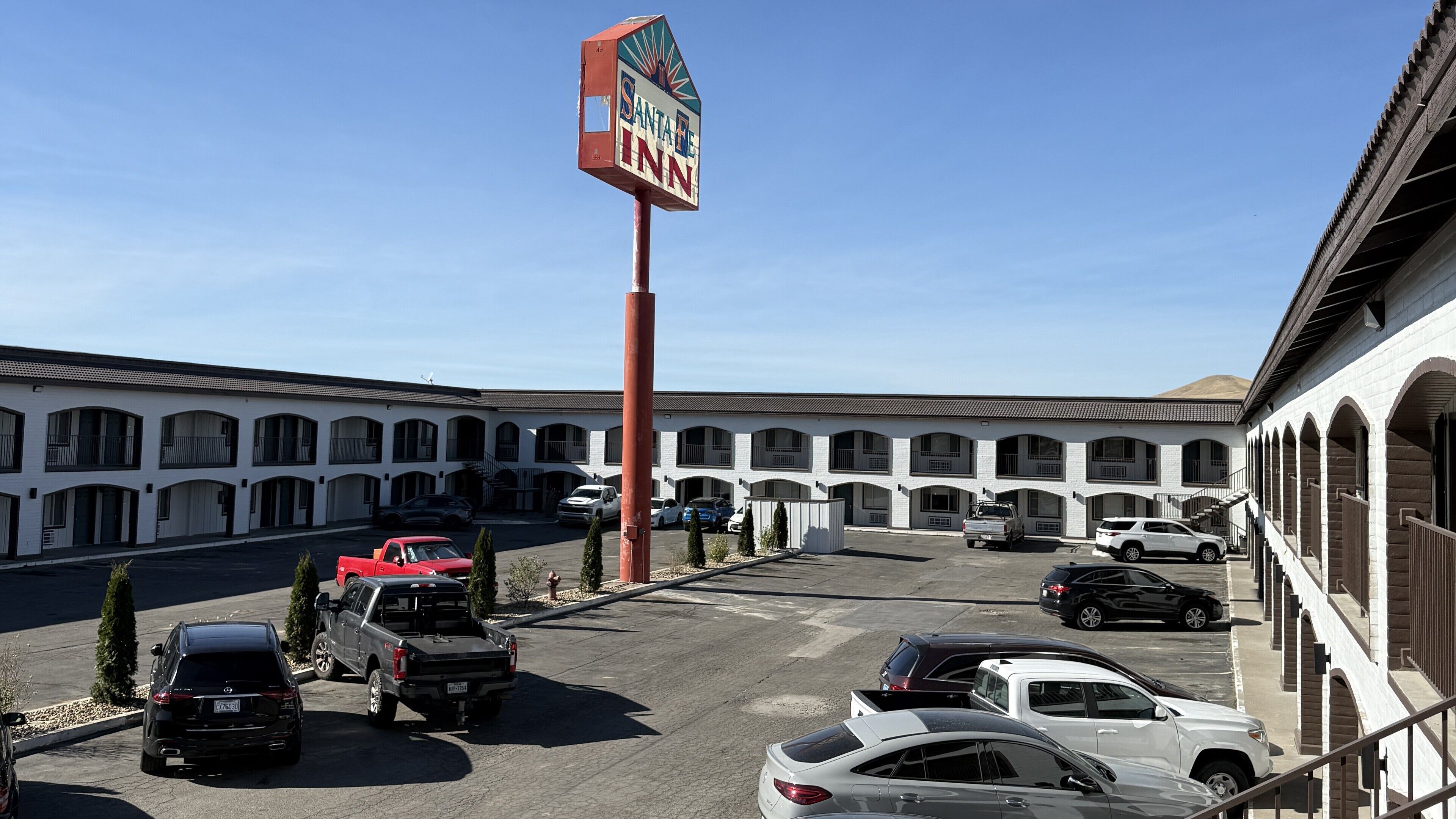 Un motel con un letrero grande, varios espacios de estacionamiento y una fila de habitaciones con ventanas arqueadas.