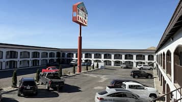 Un motel con un letrero grande, varios espacios de estacionamiento y una fila de habitaciones con ventanas arqueadas.