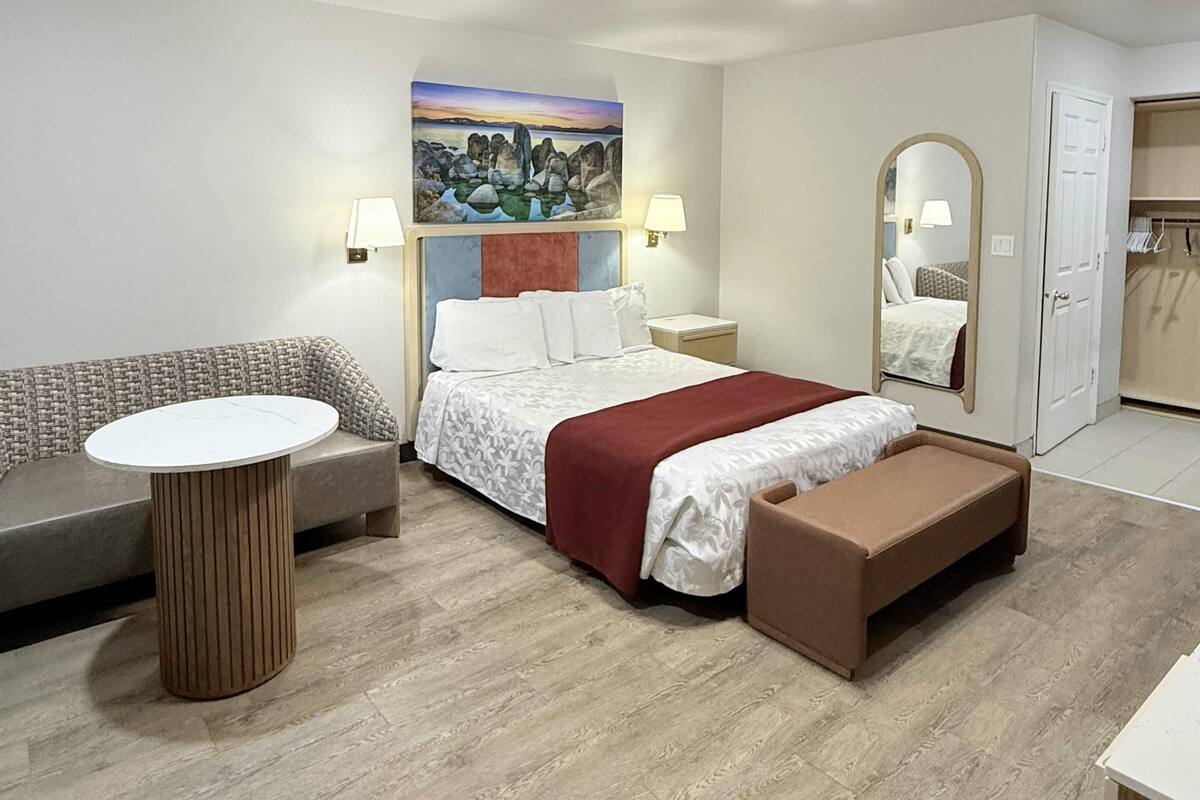 Une chambre d’hôtel moderne, équipée d’un lit, d’une table ronde, d’un banc, d’un canapé et d’un tableau au mur.