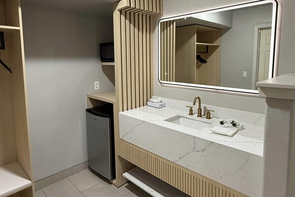 A bathroom with a white marble sink, a mirror, and a trash bin. - Rodeway Inn Winnemucca (Winnemucca)