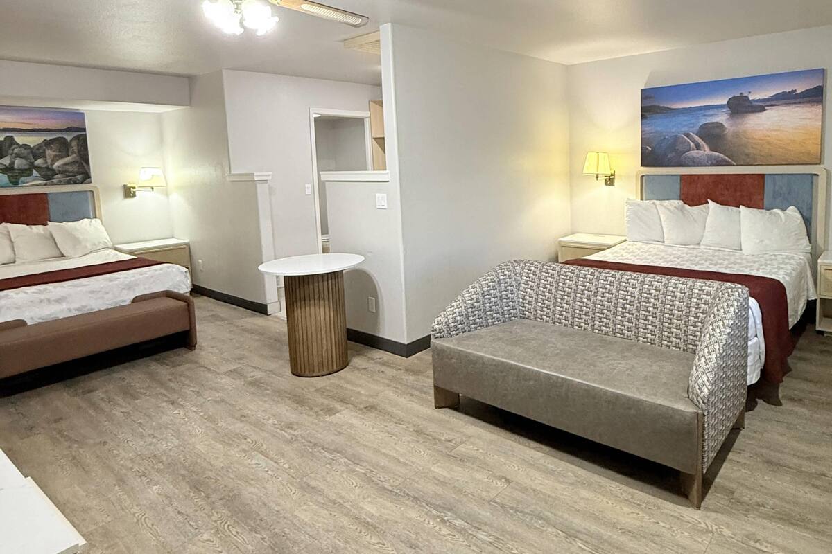 Une chambre d’hôtel avec deux lits, un canapé, une table ronde et des œuvres d’art aux murs.