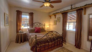 A bedroom with a bed, a ceiling fan, a bedside table with a lamp, and curtains on the windows. - Breezy Pines Cabin | Backyard Picnic | BBQ (South Lake Tahoe)