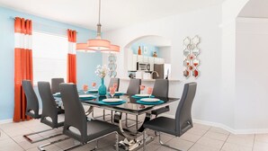 Een eetgedeelte met een glazen tafel, zwarte stoelen en oranje gordijnen.