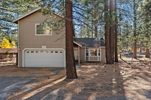 A two-story house with a garage, surrounded by tall pine trees.