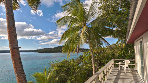 A wooden deck with a white chair, overlooking a turquoise sea and palm trees. - Mala Island Resort (Mala)