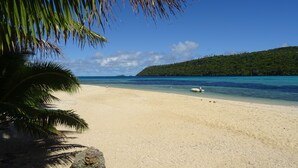 A beach with clear turquoise water, a boat on the shore, and a lush green hill in the background. - Mala Island Resort (Mala)