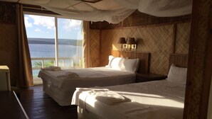 A room with two beds, a large window with curtains, a nightstand, and a lamp. - Mala Island Resort (Mala)