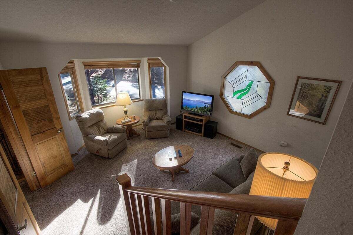 Een woonkamer met een bank, fauteuils, een salontafel, een televisie en een groot raam met uitzicht op bomen.