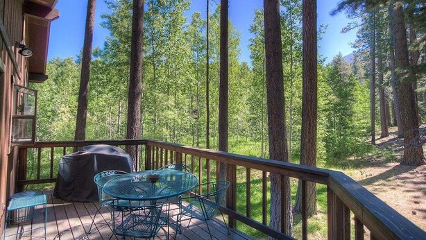 A wooden deck with a metal table and chairs, surrounded by tall trees. - Aspen View Lodge | BBQ | 2 Miles from Heavenly Ski (South Lake Tahoe)