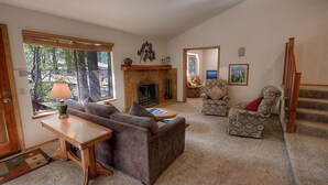 A cozy living room with a fireplace, a sofa, a patterned armchair, and a wooden coffee table. - Aspen View Lodge | BBQ | 2 Miles from Heavenly Ski (South Lake Tahoe)